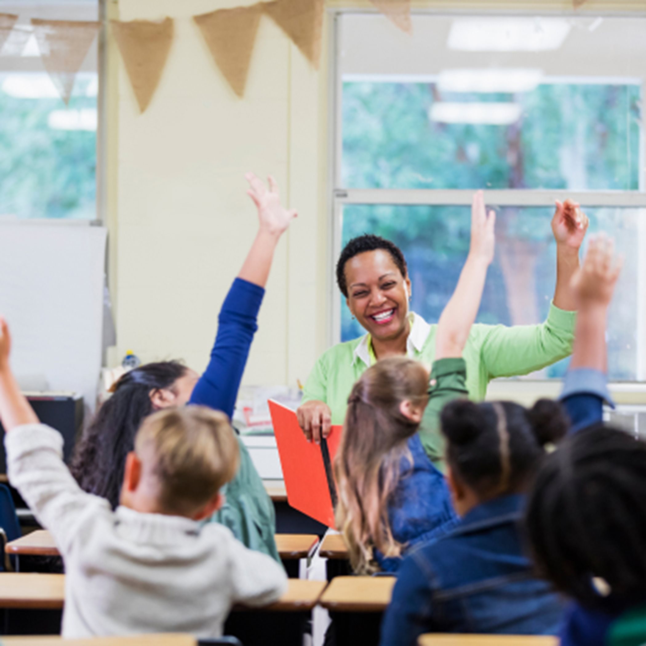 A teacher with elementary students raising their hands