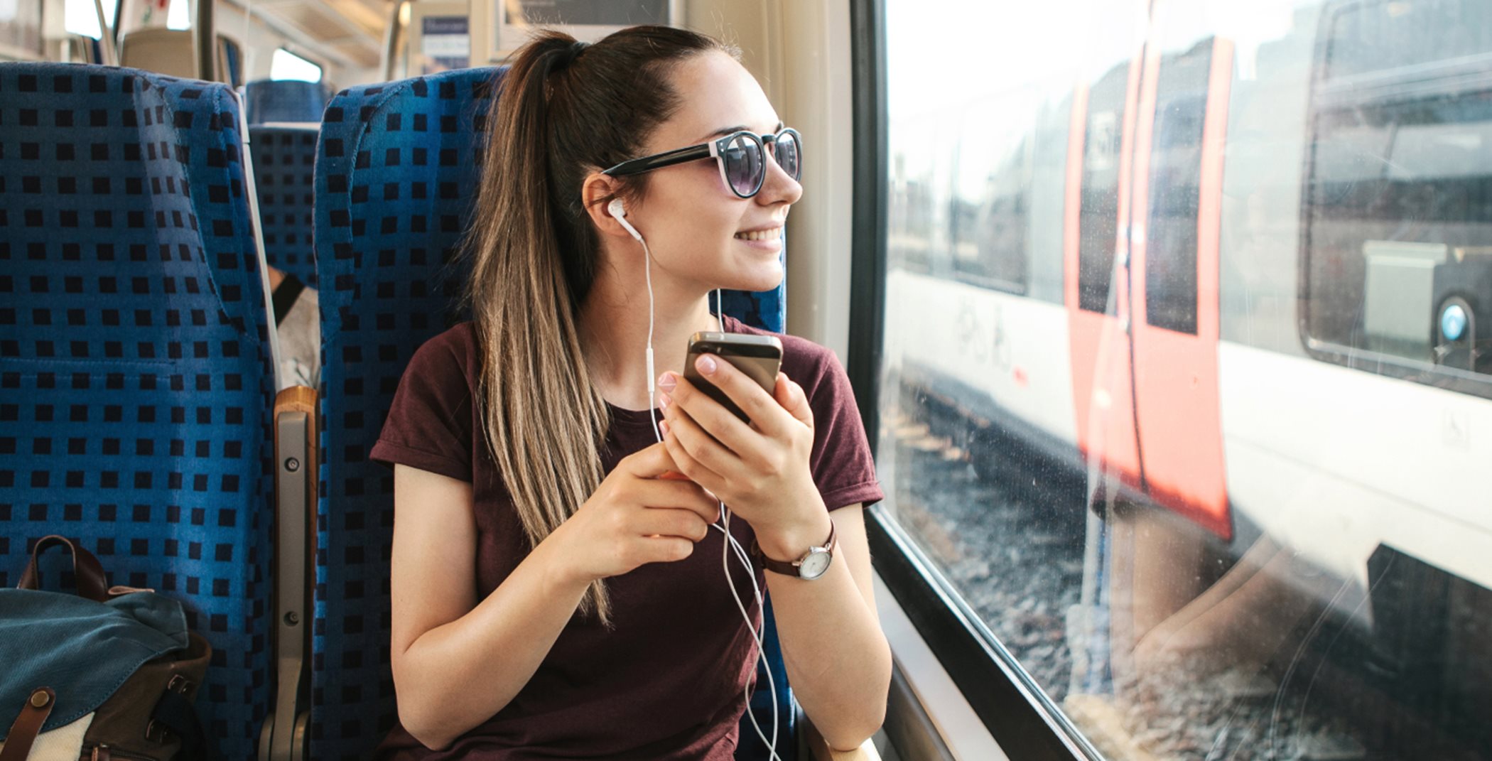 A person sitting on a train listening to their phone with headphones