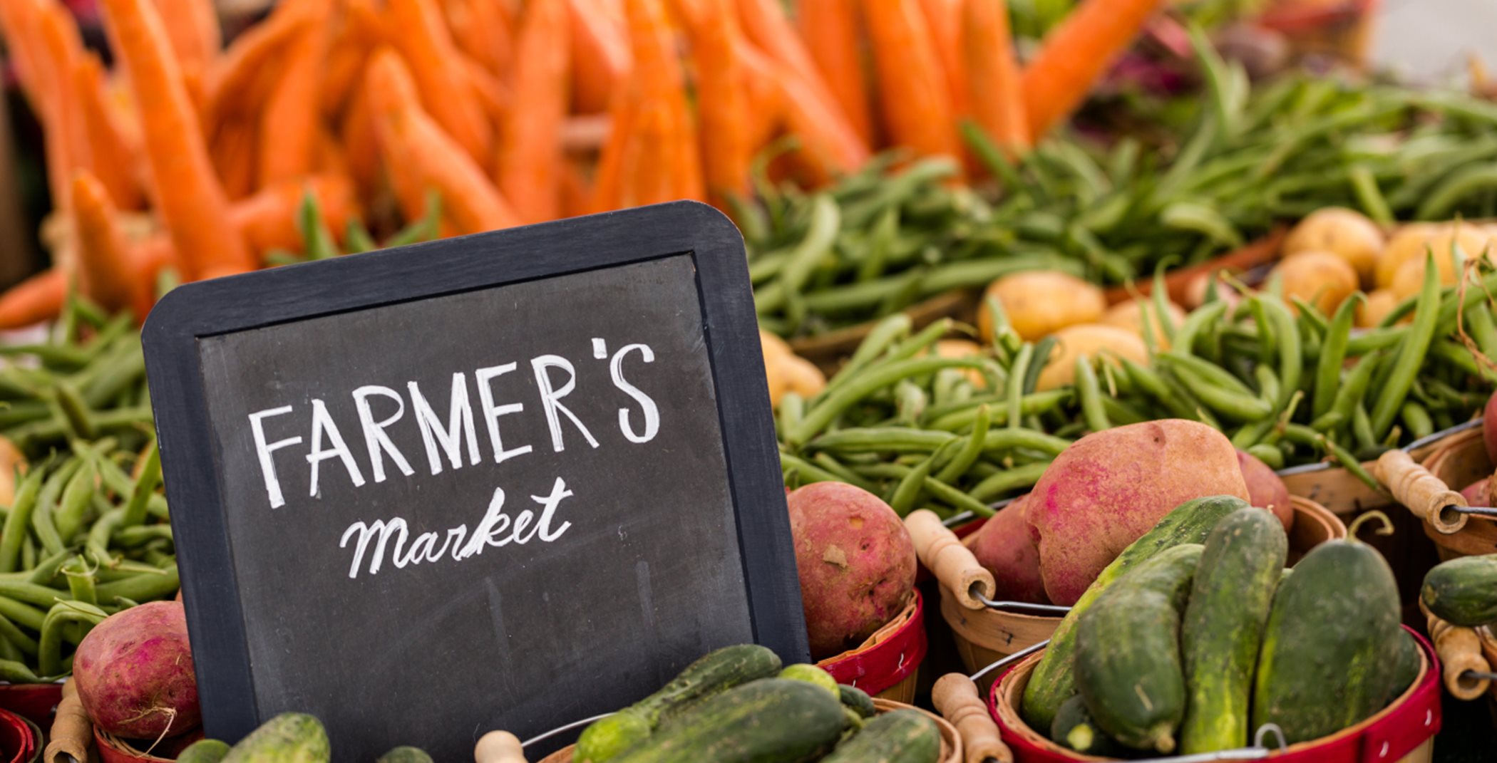 A chalkboard sign that says Farmer's market surrounded by vegetables