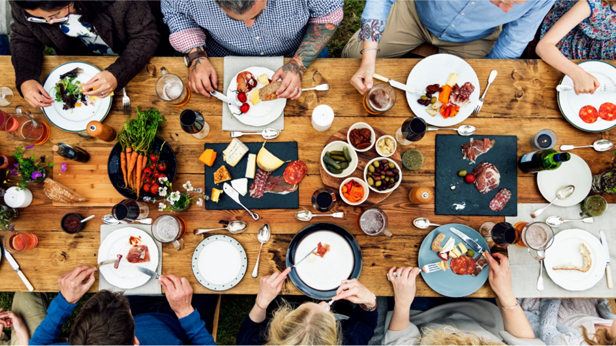 Overhead view of people enjoying a potluck style meal at a wooden table