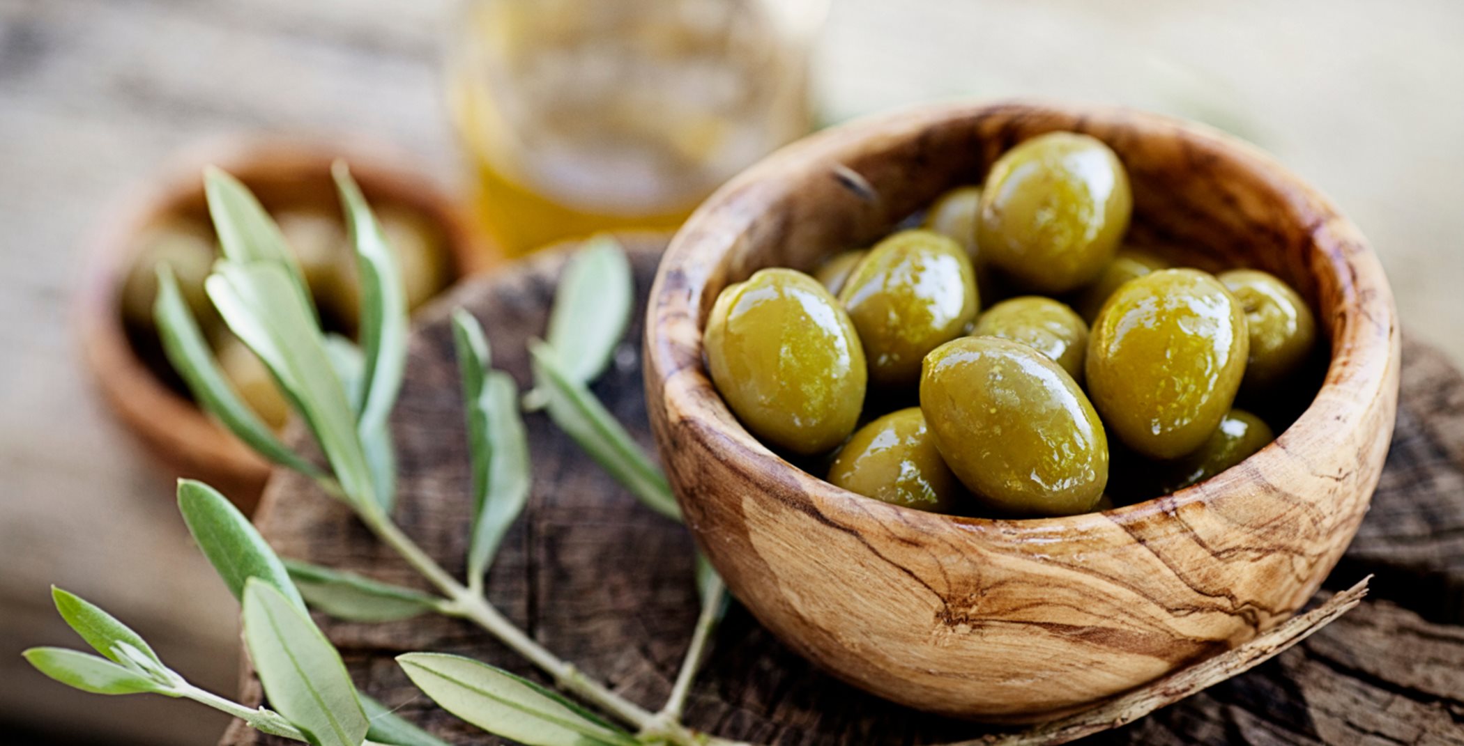 Bowl of olives next to an olive branch on a table