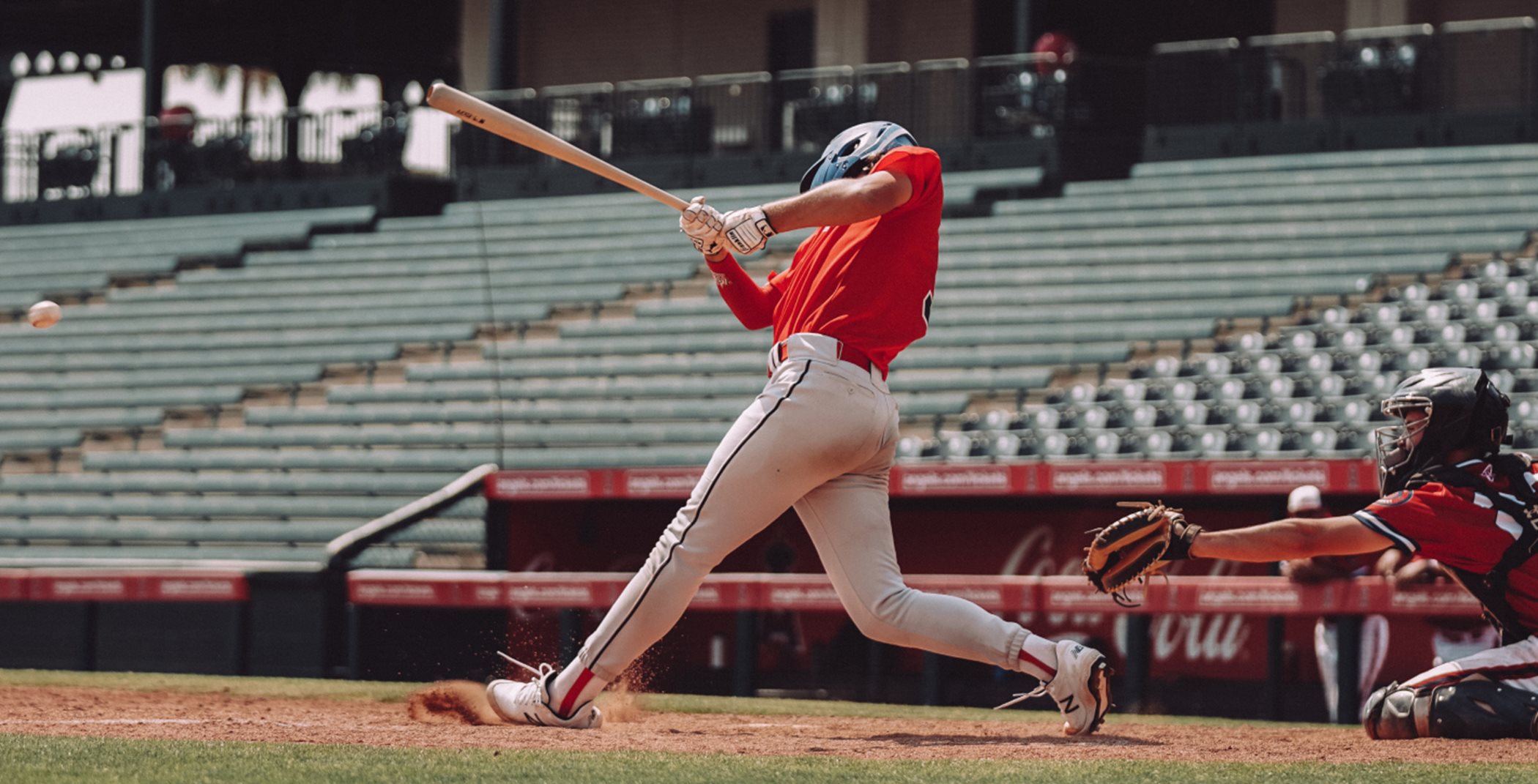 Two baseball players. One is swinging the bat while the other sits behind him, poised to catch the ball.
