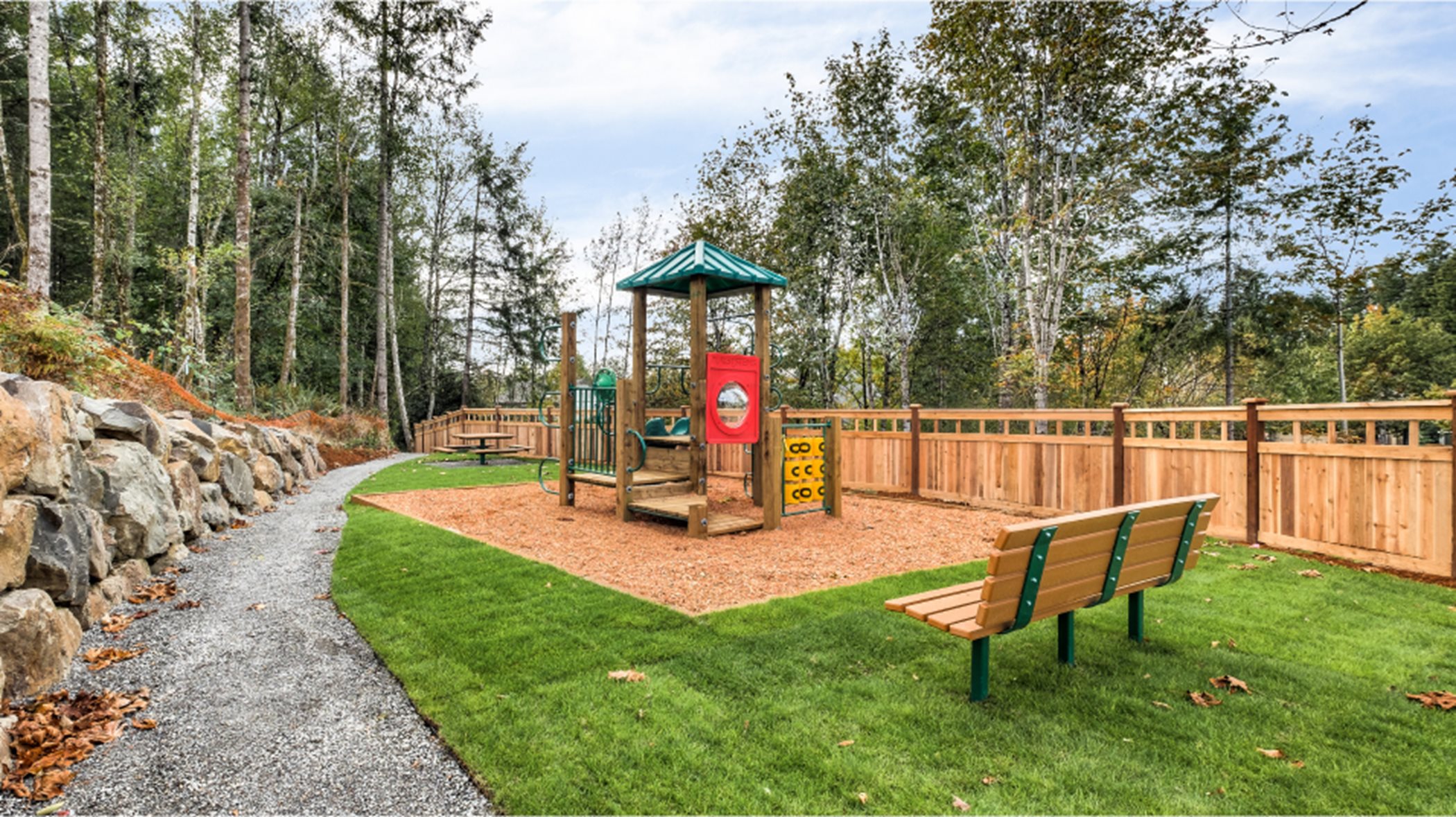 A park with a patch of grass, a playset and a bench