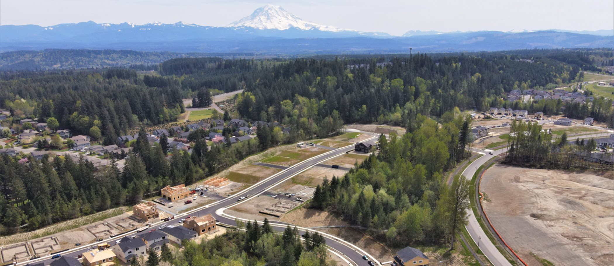An aerial view of the community with several pine trees and homes with a snow covered mountain top in the background