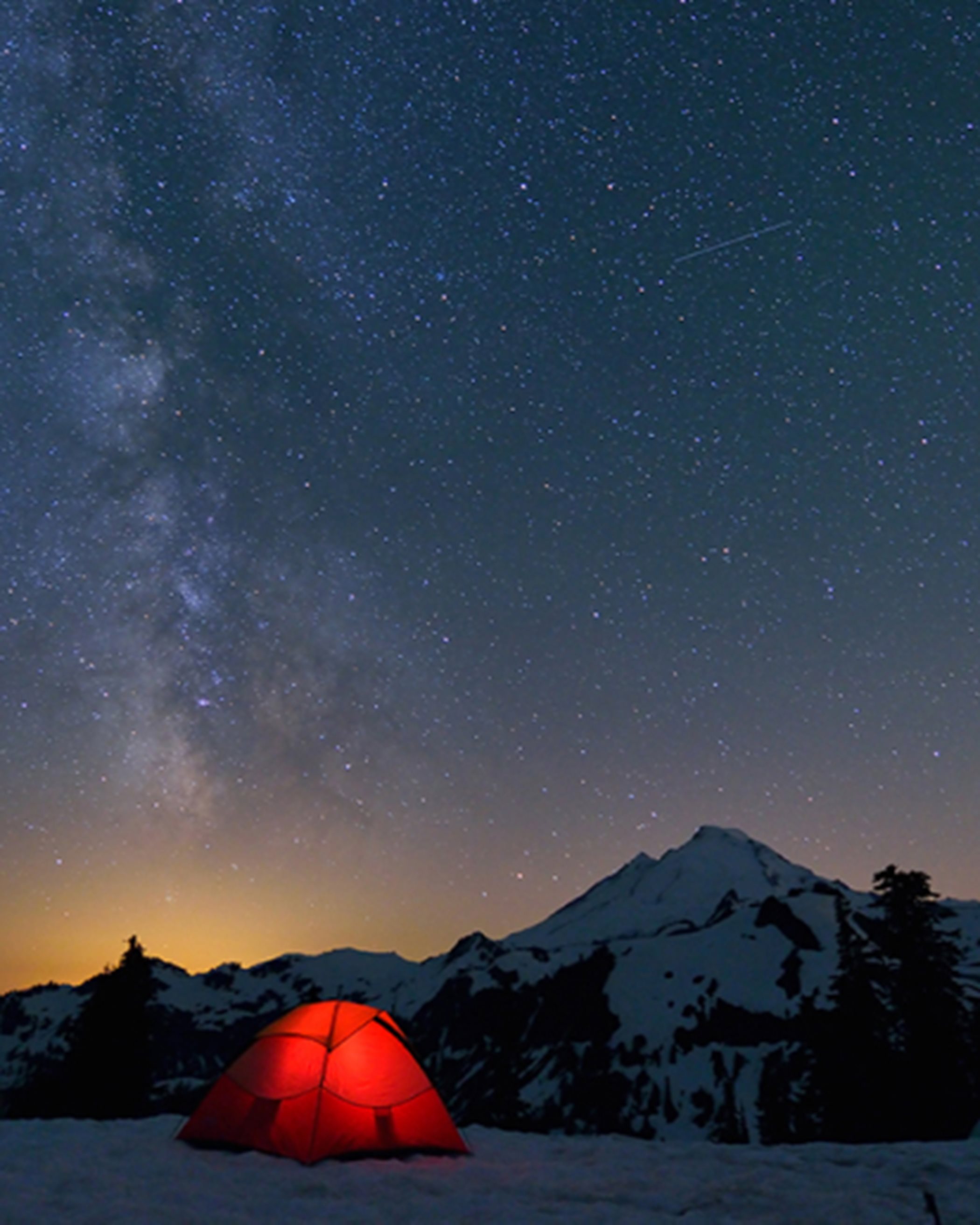 A red tent sits among snowy mountains and twilight night with lots of stars