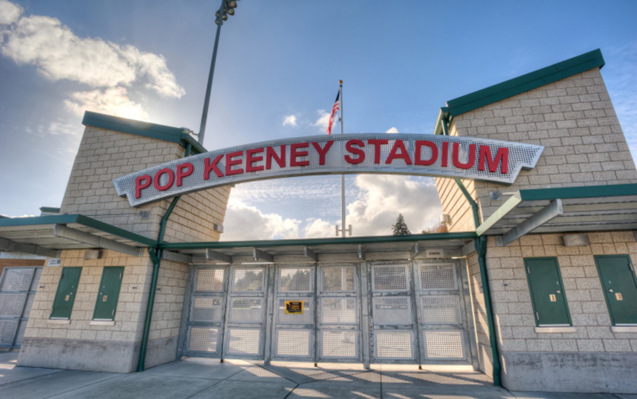 A stadium with the pop keeney sign held by two towers/ticket booths made of tan brick with green accents