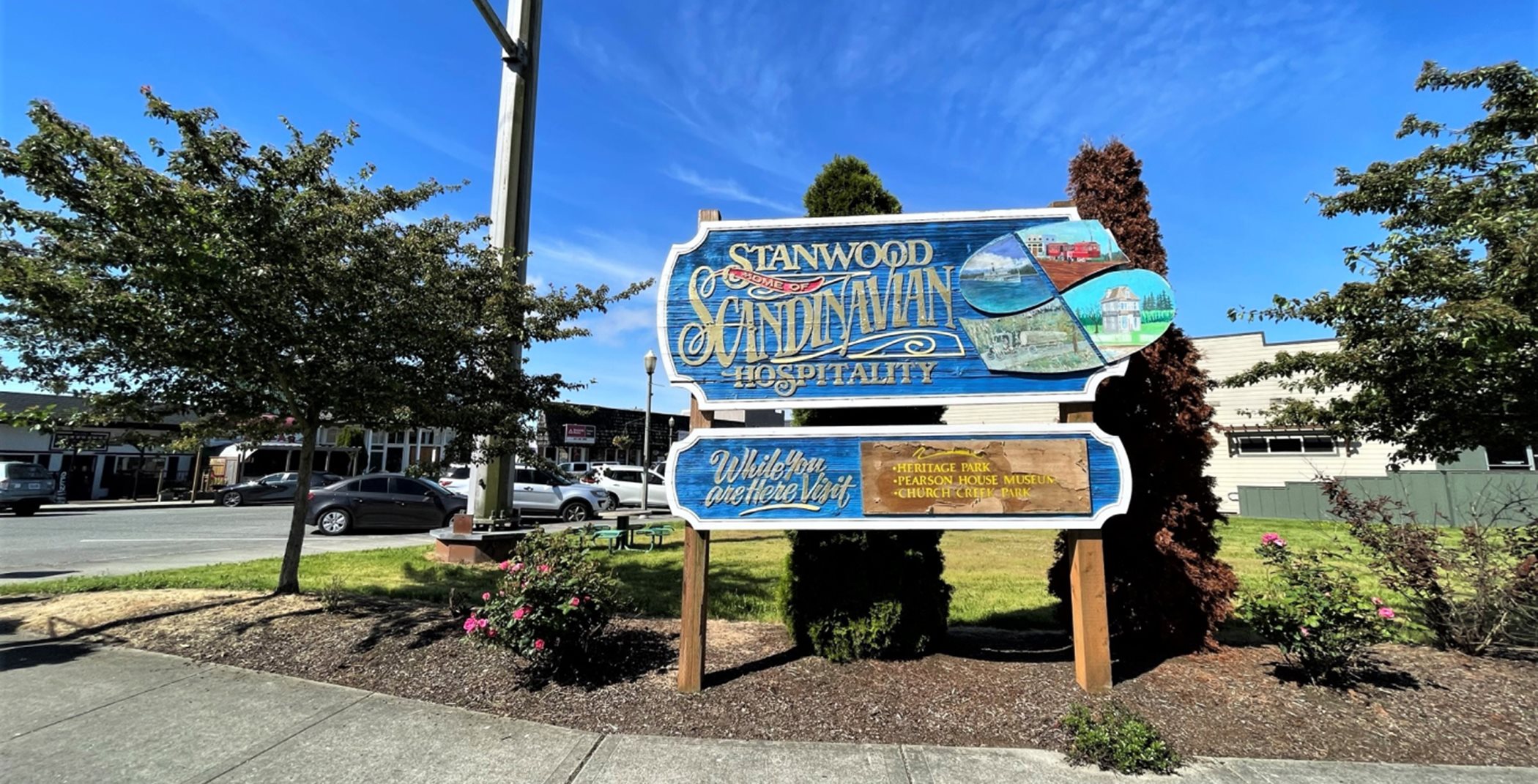 Stanwood welcome sign. It is blue with pale yellow cursive lettering. The sign reads:  Stanwood - Home of Scandinavian Hospitality