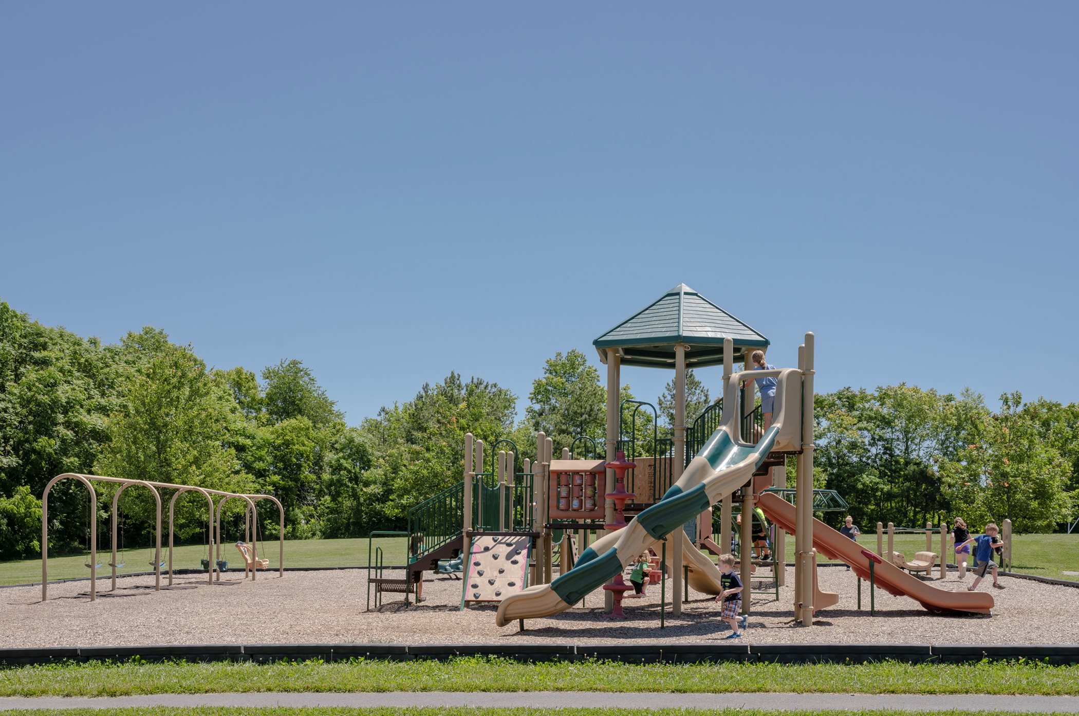 A play set surrounded by trees that features two slides and a rock-climbing wall