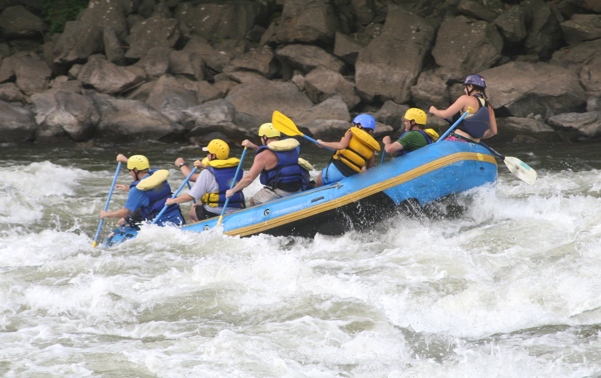 A group of people on a raft guide the boat through white splash with rocks in the background