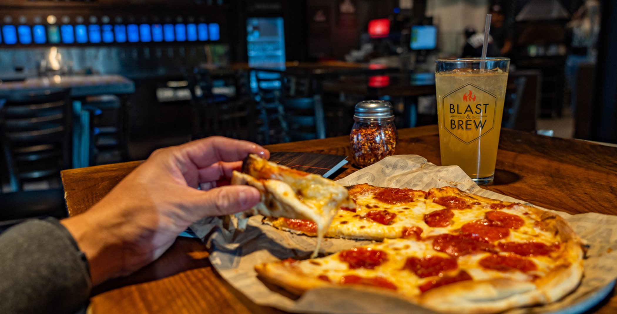 Man holding pizza slice with blast and brew beer