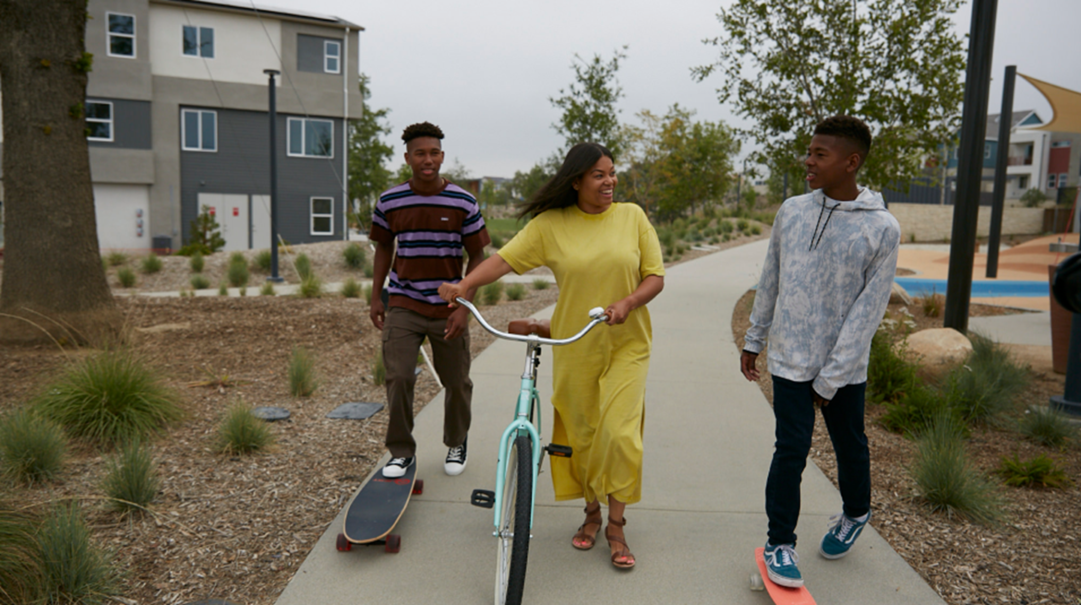 Three residents walking bikes and skateboards on a community trail