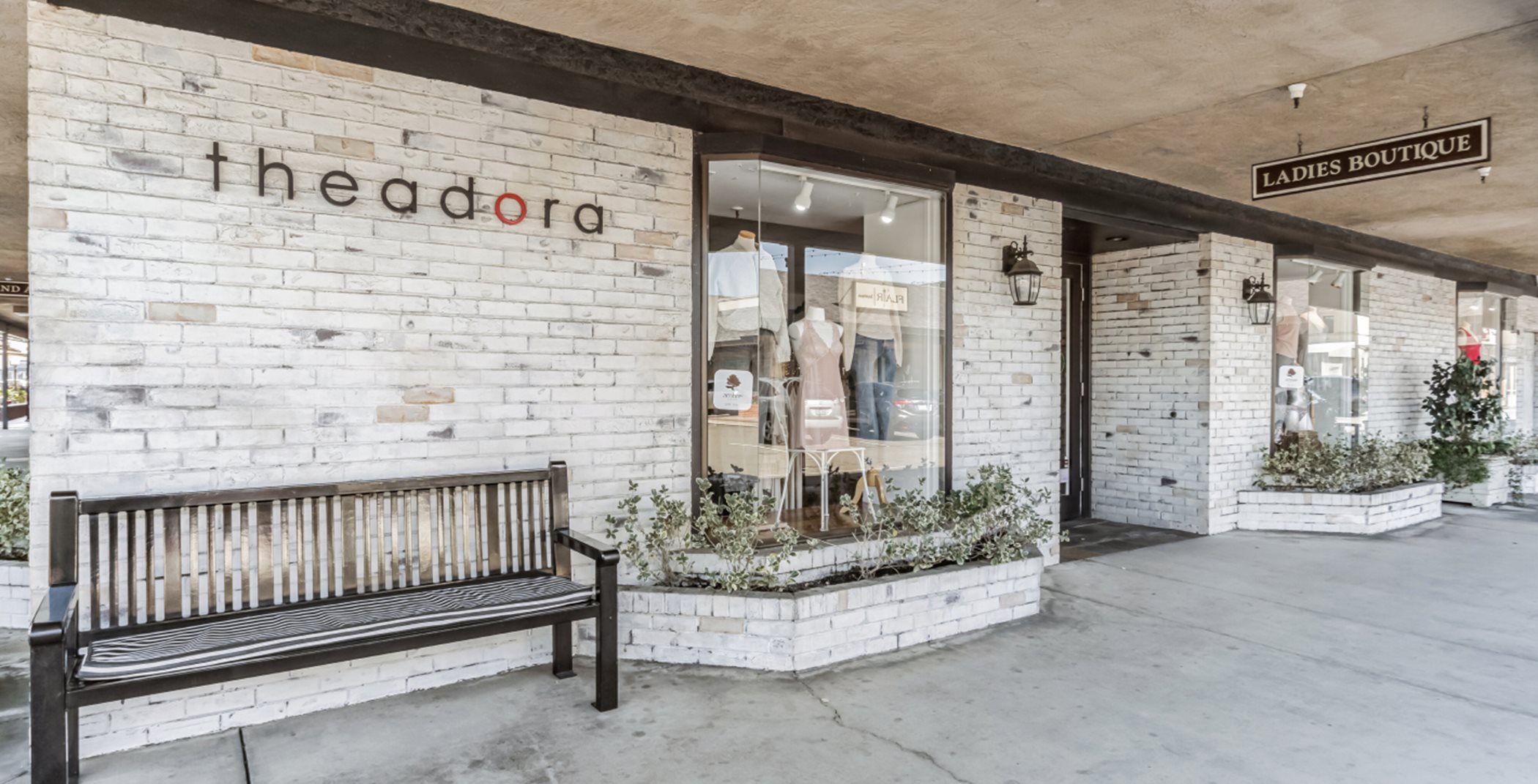 Exterior of the Theodora Boutique storefront. It has white brick and a metal lettering that reads, "theodora."