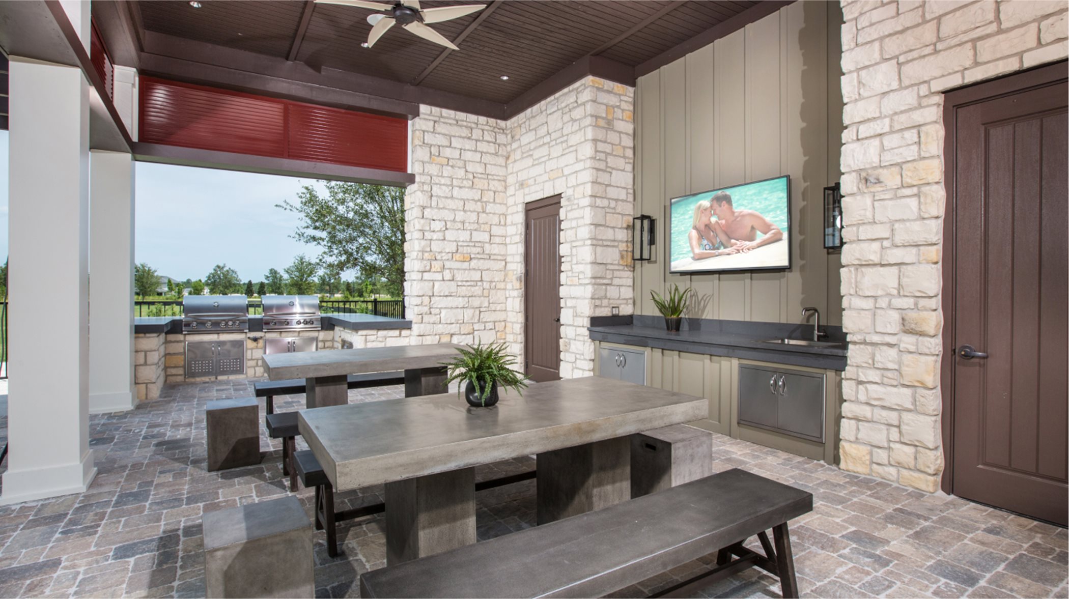 Outdoor grill area with BBQ stations, tables and Tv atop the sink
