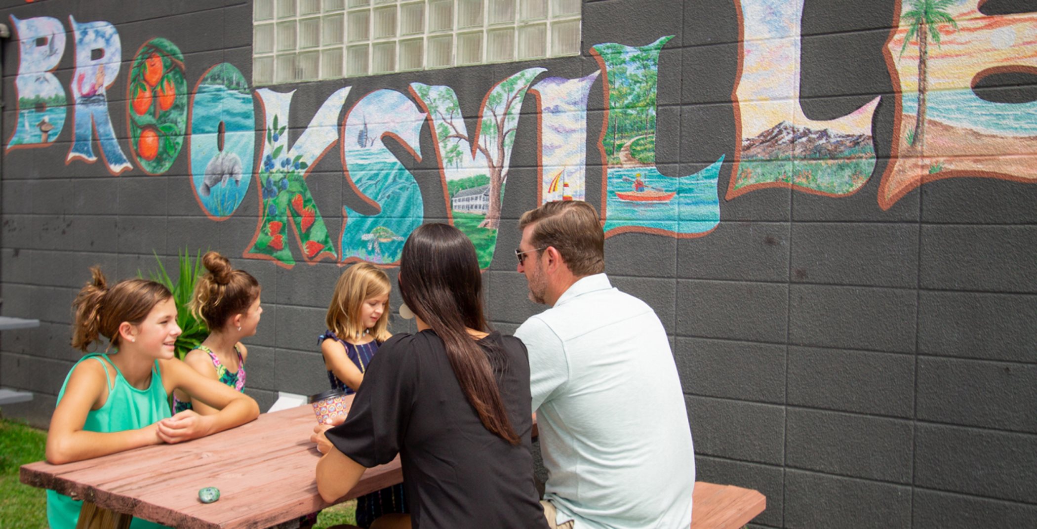 People sitting at a picnic table in front of Brooksville art wall