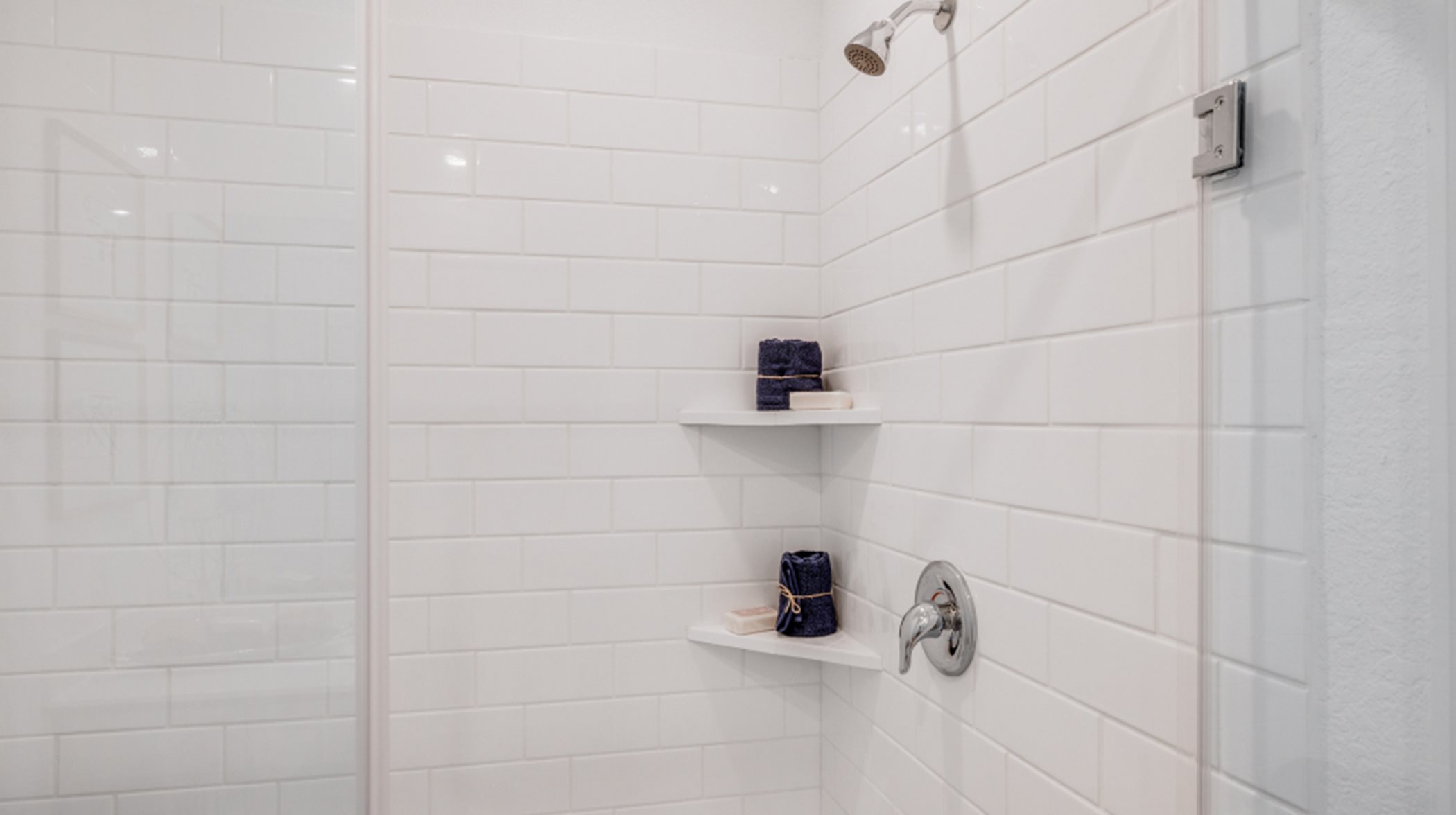 Glass-enclosed shower with subway tile surround and built-in shelving 